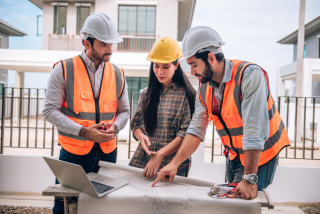 Engenheiro civil e arquitetos usando capacetes e coletes de segurança estão trabalhando juntos na obra