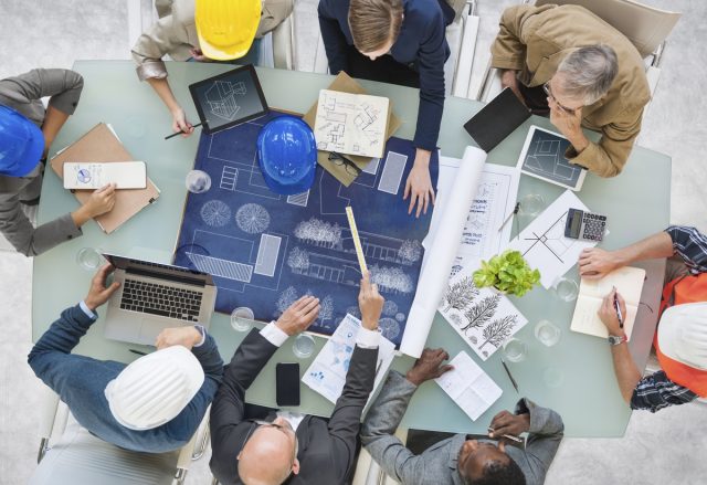 Visão de cima de uma mesa com um grupo de pessoas sentados em volta planejando obra