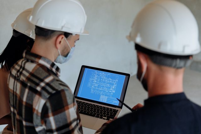 Imagem de trabalhadores da construção civil olhando para informaçoes em um notebook