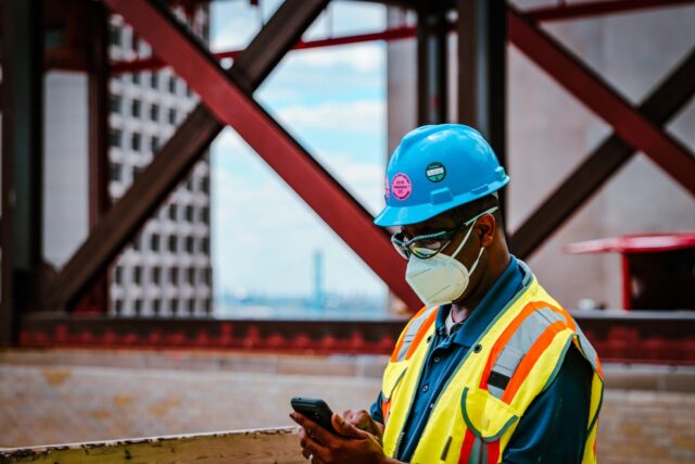 homem com EPIs finalizando um obra e olhando no seu celular